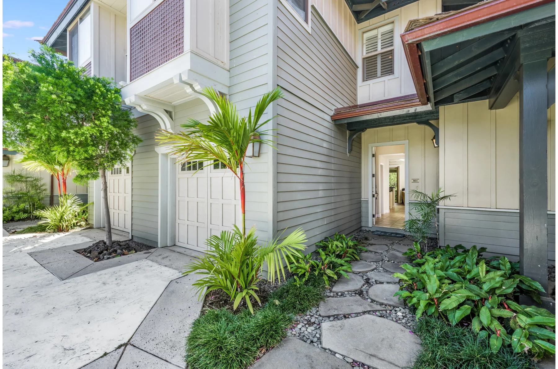 A paved courtyard beside a light-colored building, with tropical plants and an open passage.