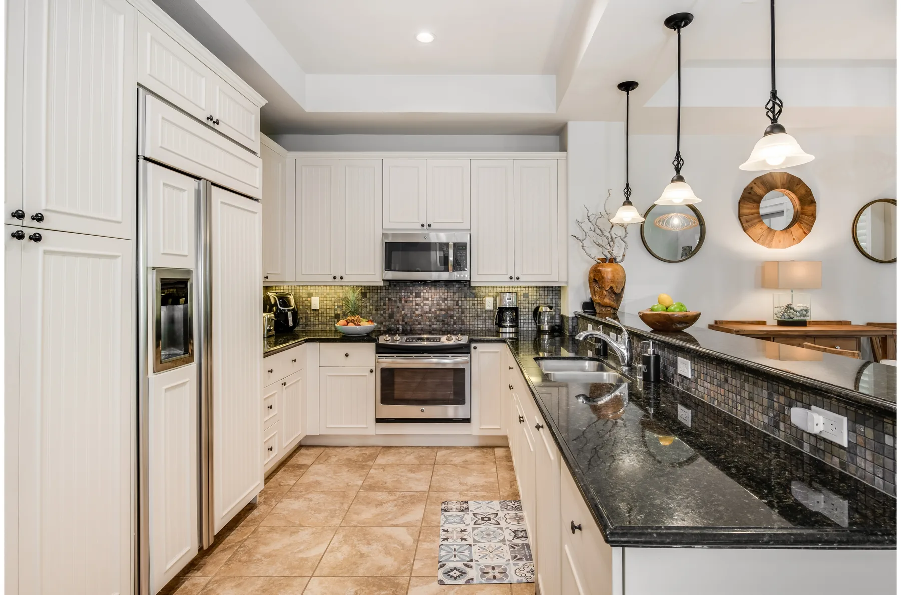 A bright kitchen with white cabinetry, dark countertops, and pendant lights.
