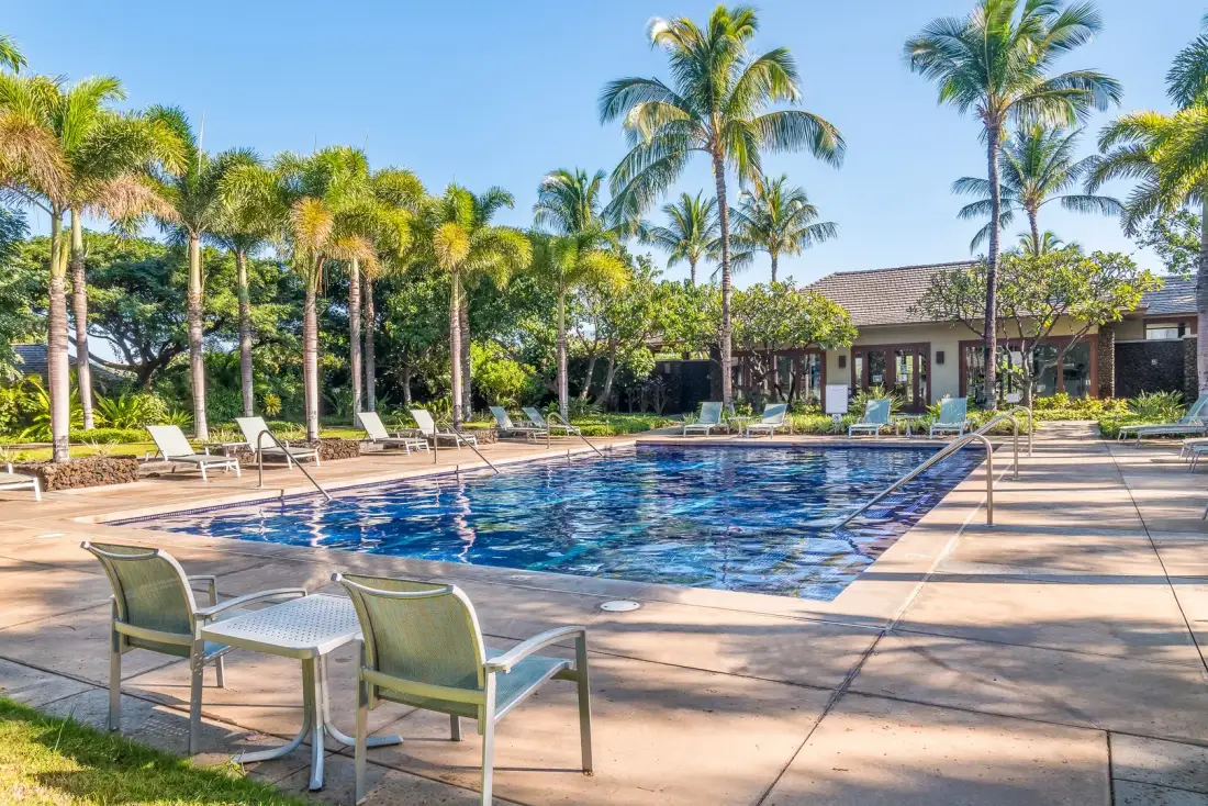 An outdoor swimming pool is surrounded by lounge seating and palm trees.