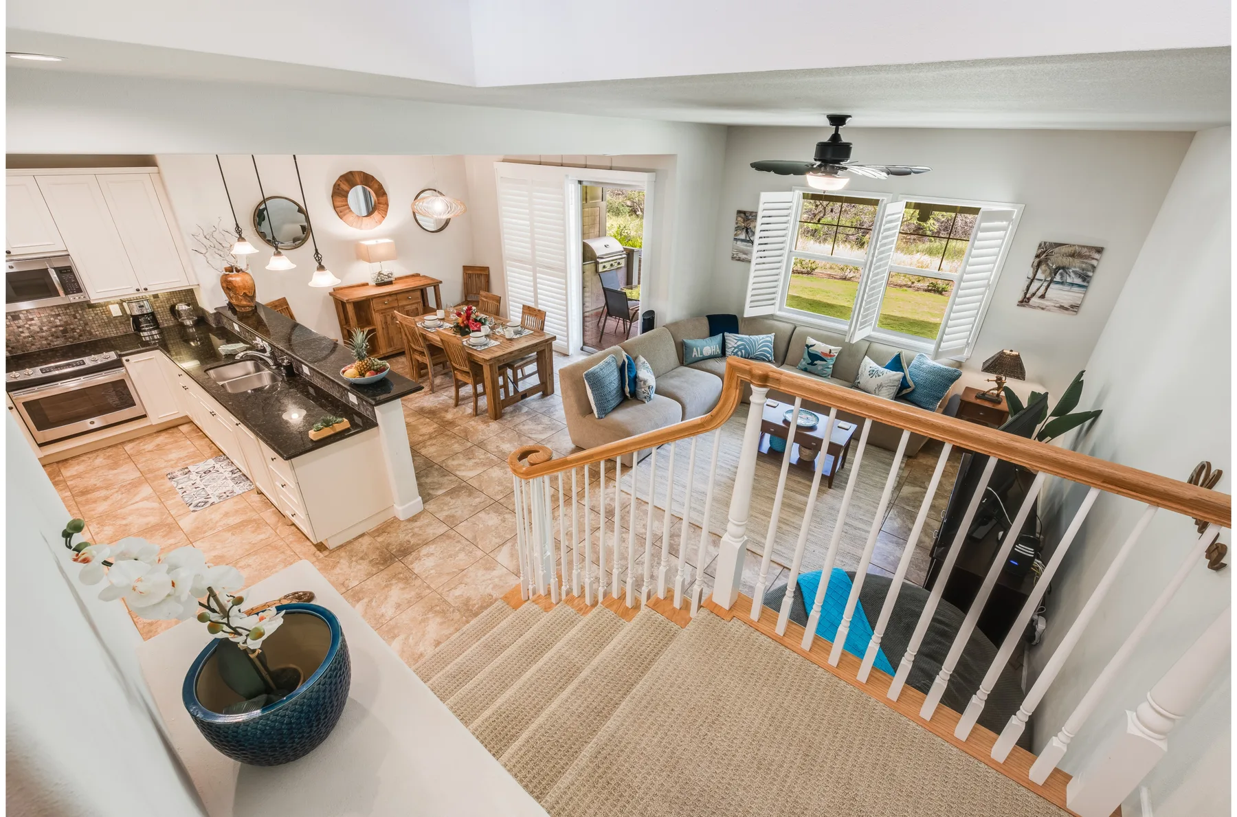 An open-plan living room and kitchen overlook a staircase with white railings.