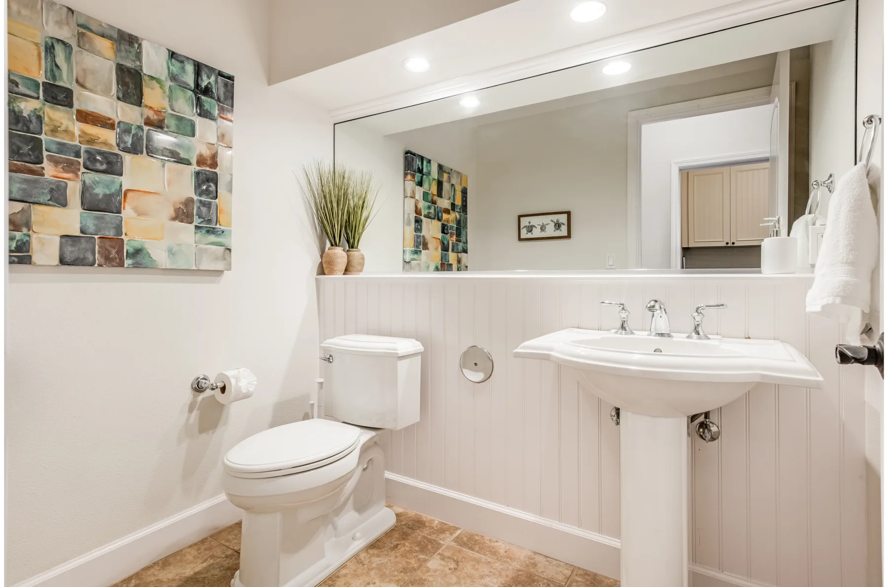 A bright bathroom with a toilet, sink, and colorful tiled wall art.