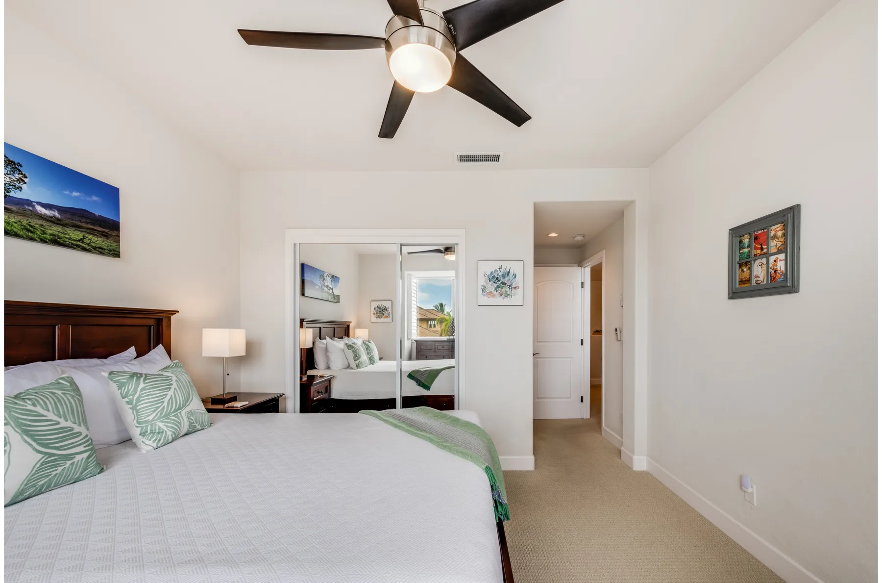 A bright bedroom with a bed, ceiling fan, and mirrored closet doors.