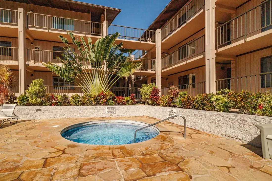 Un patio exterior con una piscina pequeña, pavimento de piedra y balcones alrededor.