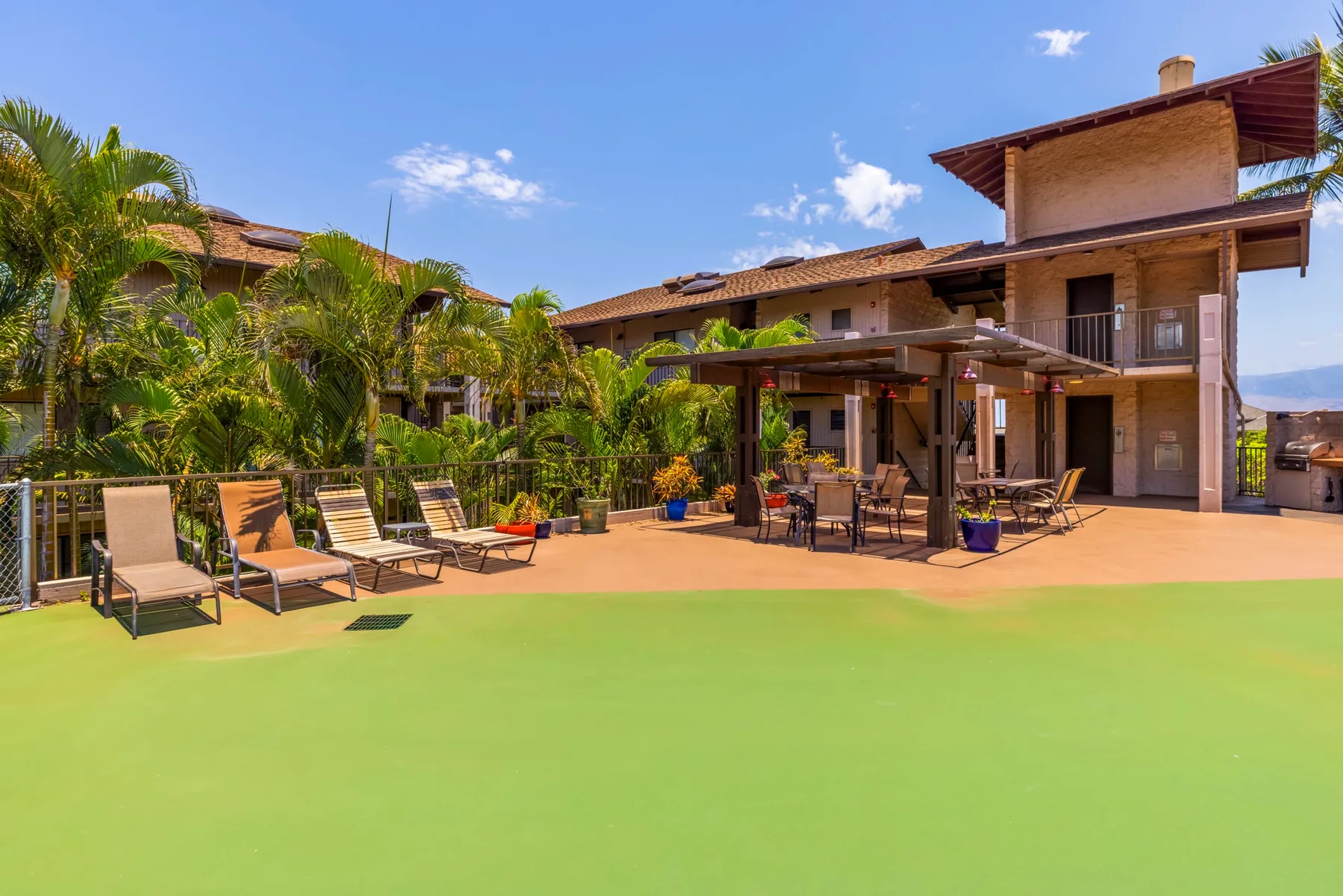 Un patio al aire libre junto a una casa grande, con asientos de descanso y plantas tropicales.