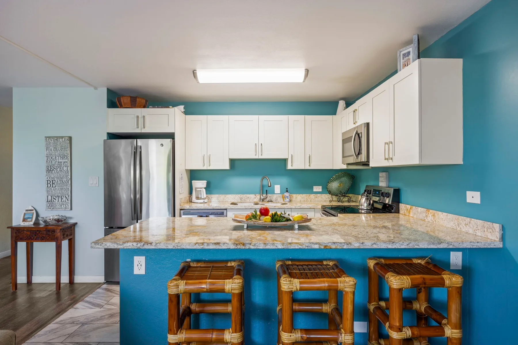 Una cocina luminosa con gabinetes blancos, una encimera de piedra y asientos de barra.