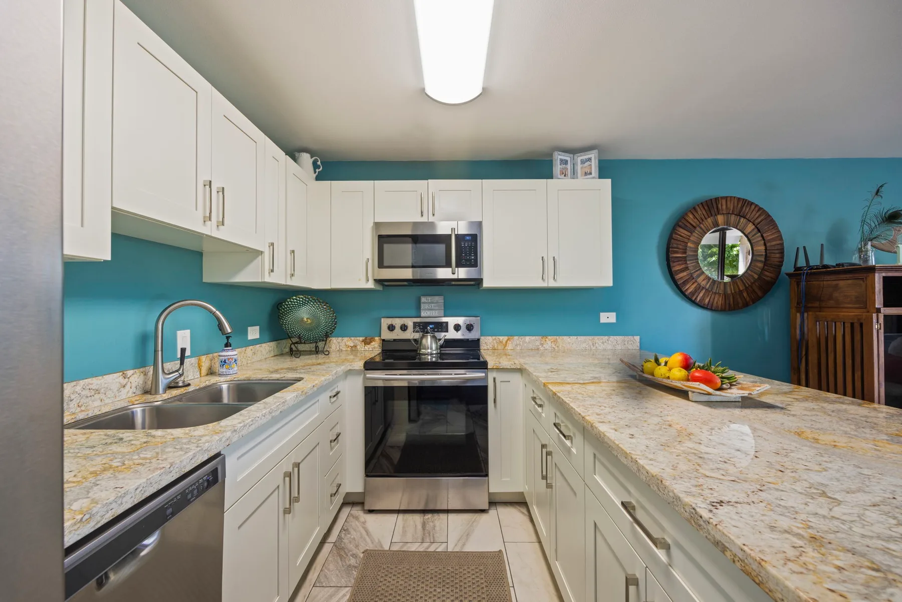Una cocina luminosa con gabinetes blancos, encimeras de piedra y una estufa central.
