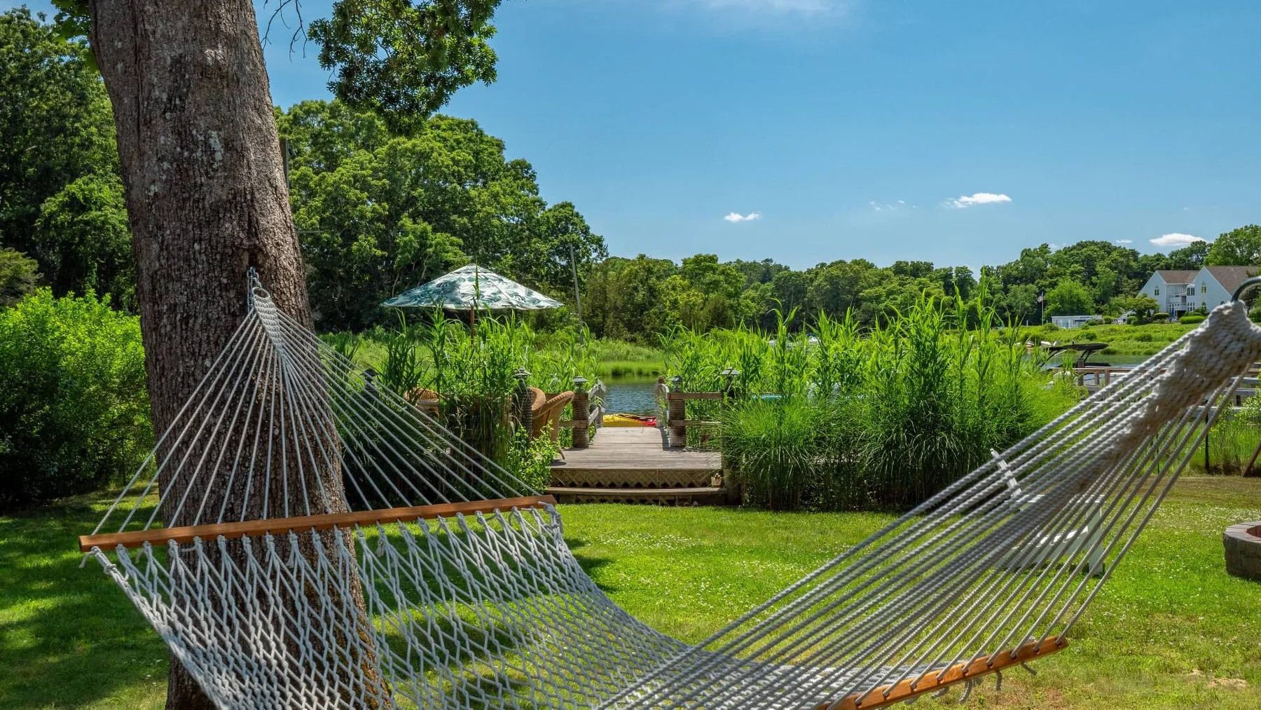 A hammock hangs beside a grassy garden overlooking a pond.