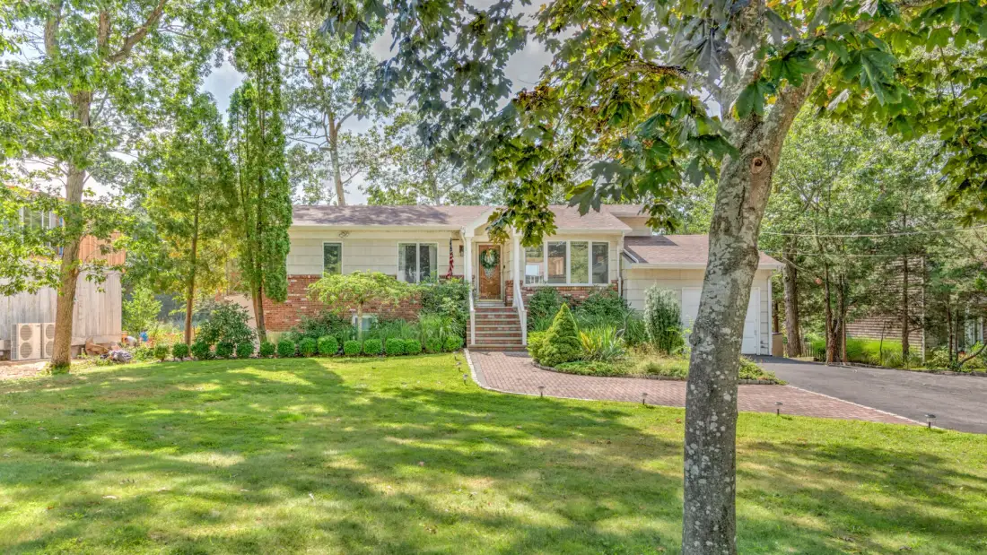 A house sits behind a green lawn, with trees and a curved walkway.