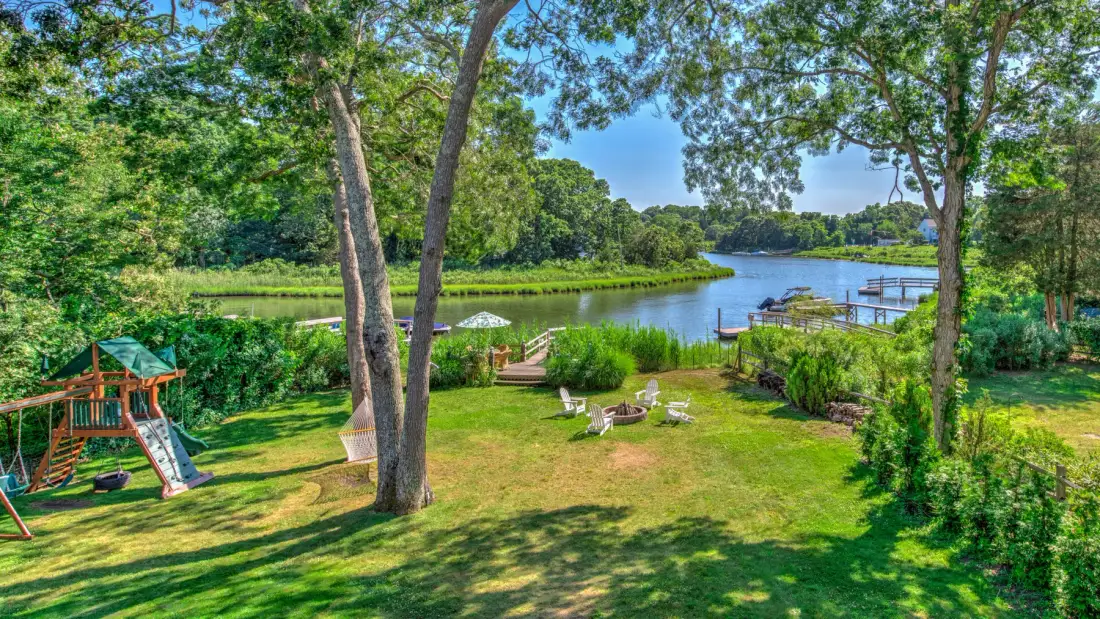 A grassy yard with a playground beside a river and dock.