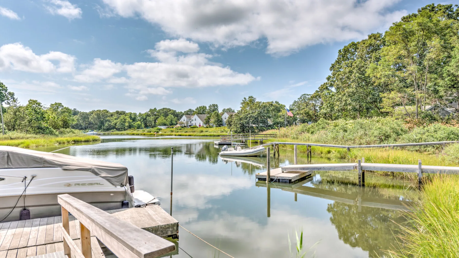 A lakeside dock extends over calm water beside a moored boat and green shoreline.
