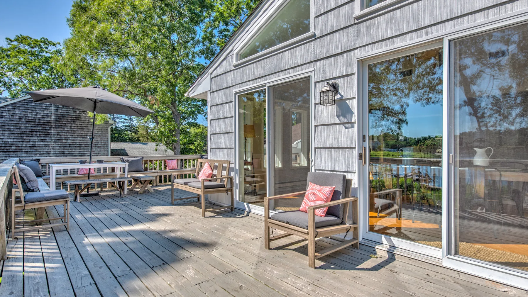 A wooden deck with outdoor seating and large glass doors beside a leafy view.