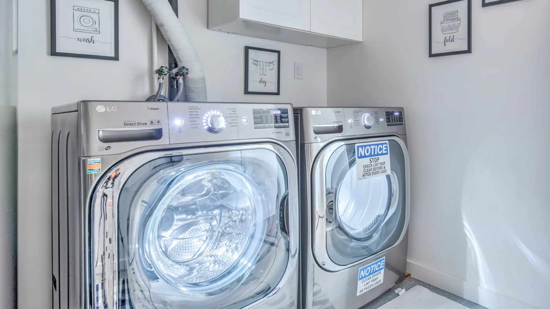 A laundry room with a front-loading washer and dryer beneath wall cabinets.