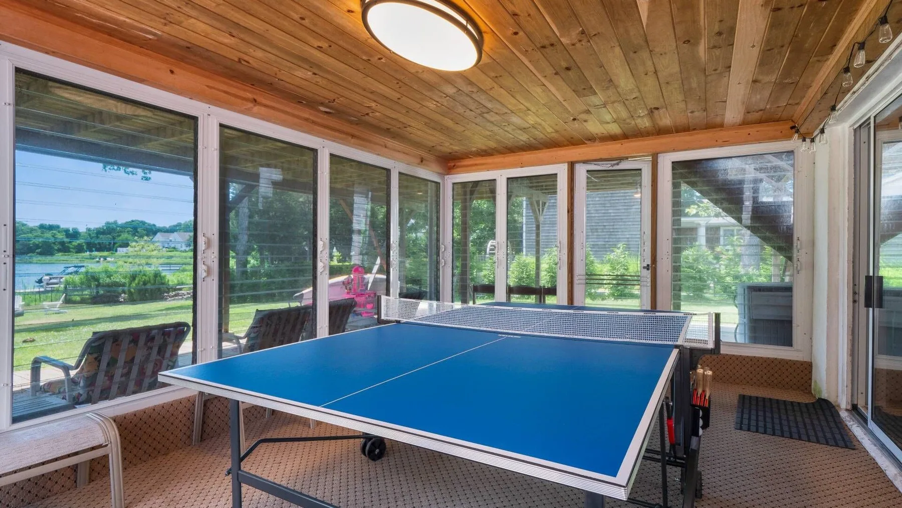 An enclosed sunroom with a blue ping-pong table and large windows.