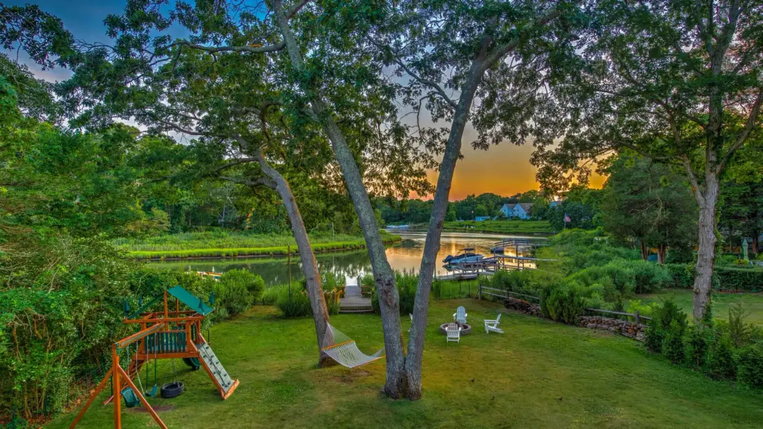A grassy garden with a small play structure overlooks a pond at sunset.