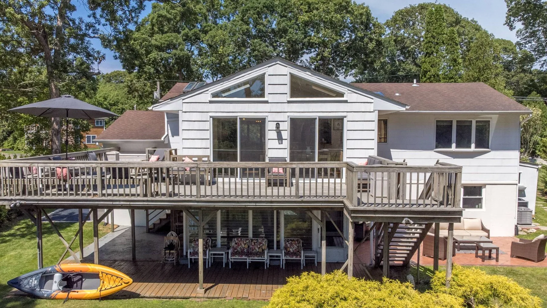 A house with a raised wooden deck, outdoor seating, and a kayak on the lawn.