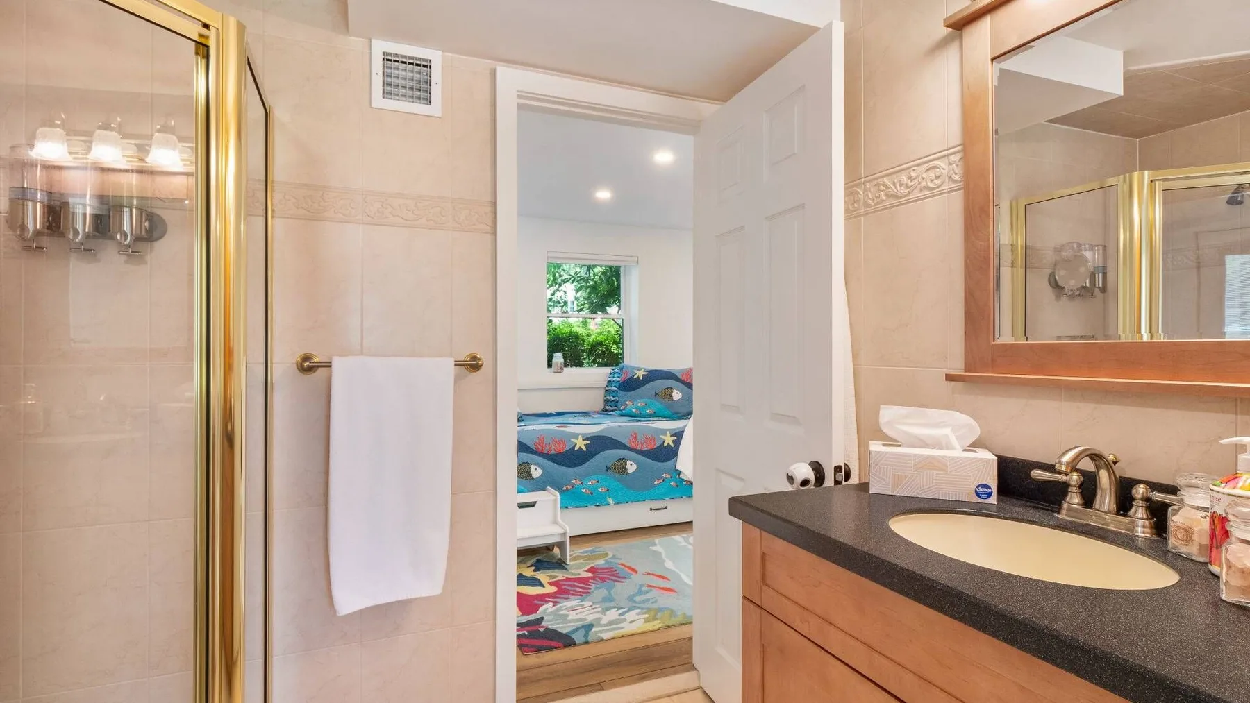 A bathroom with a sink and mirror, opening onto a bedroom with colorful bedding.