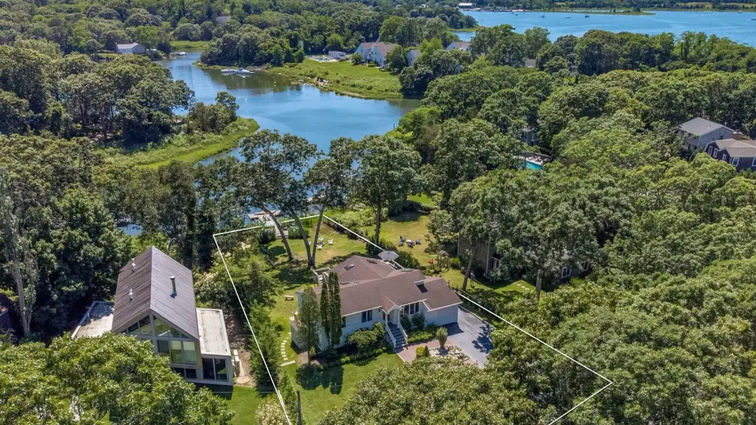 Aerial view of a house surrounded by trees, with a pond nearby.