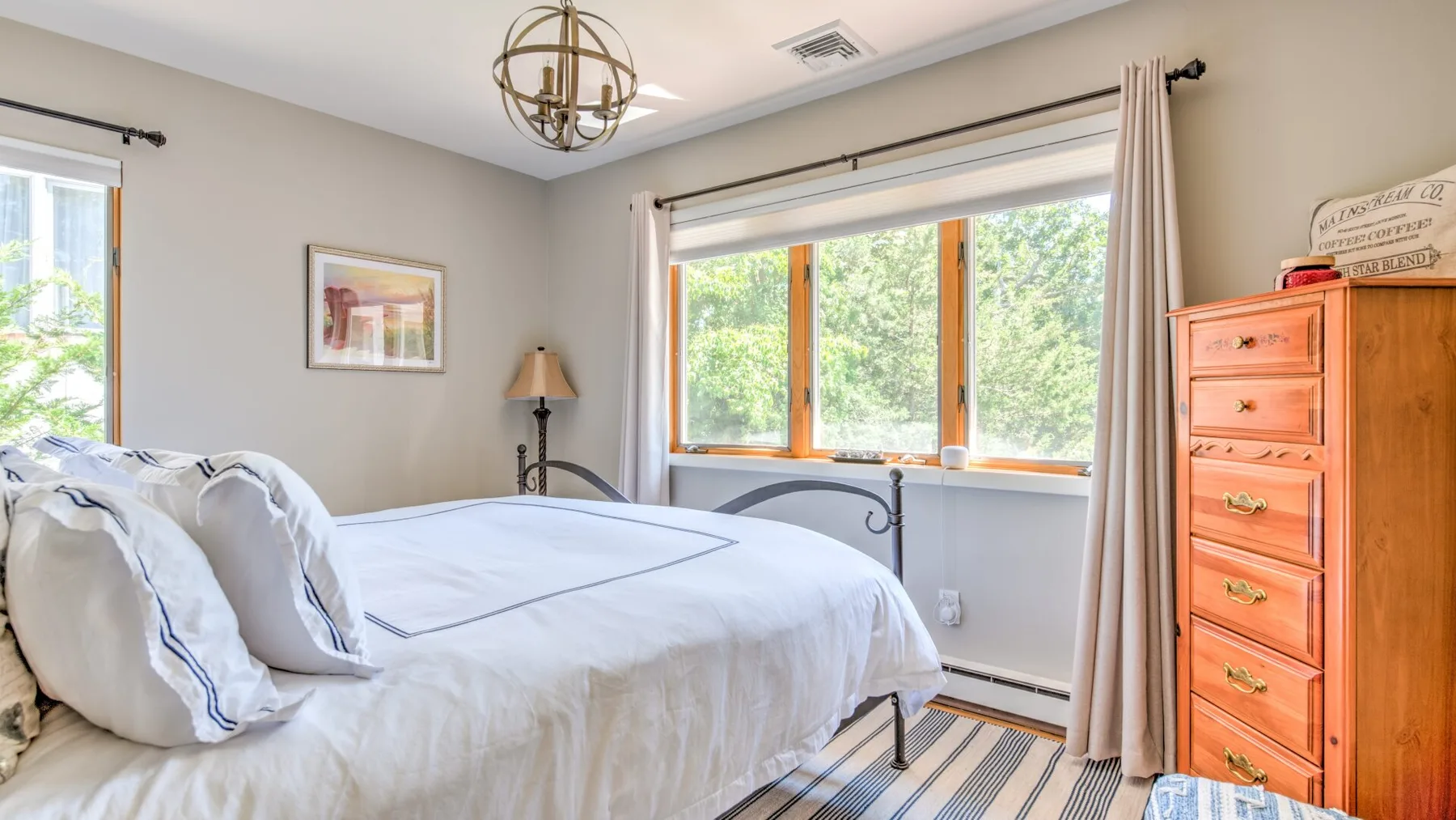 A bright bedroom with a neatly made bed and large windows overlooking greenery.