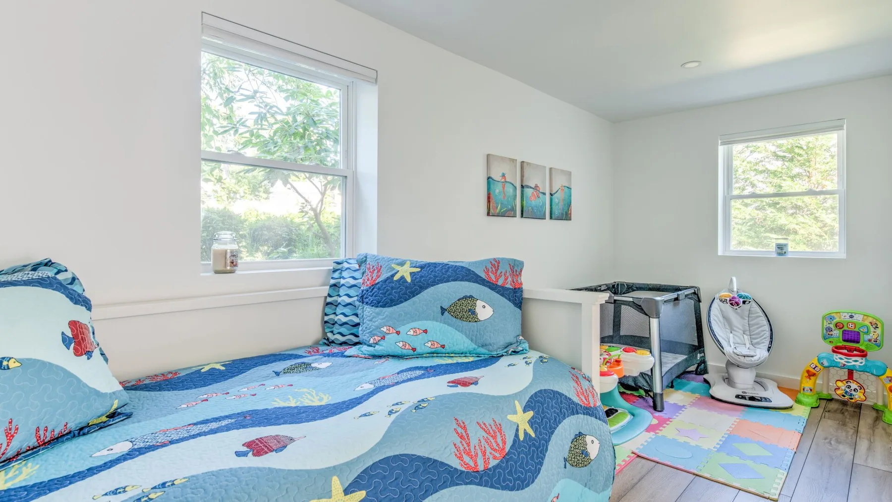 A bright bedroom with colorful bedding and a play area by the windows.