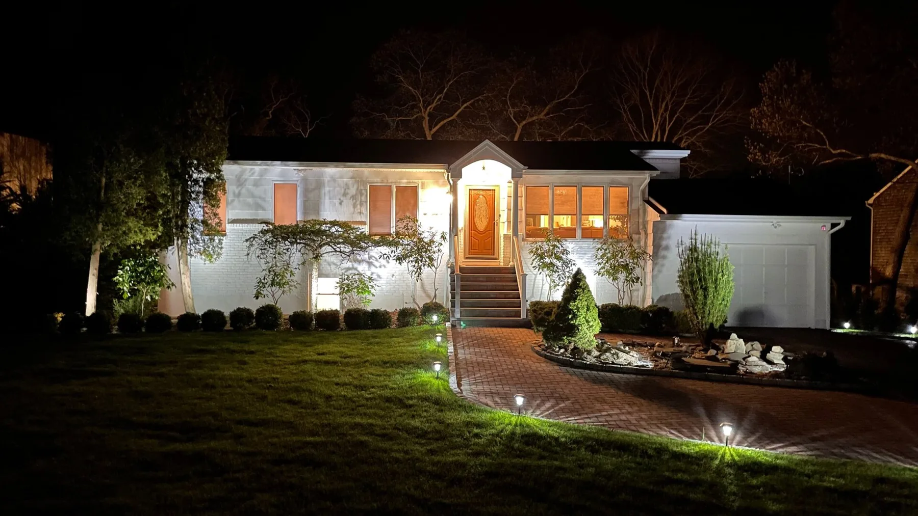 A single-story house at night, with a lit entrance and curved driveway.