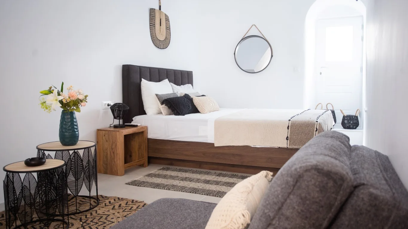 A bright bedroom with a bed, a gray seating area, and a small table with flowers.