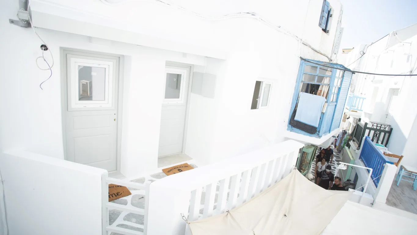 A white exterior walkway overlooks a lower courtyard with blue shutters.