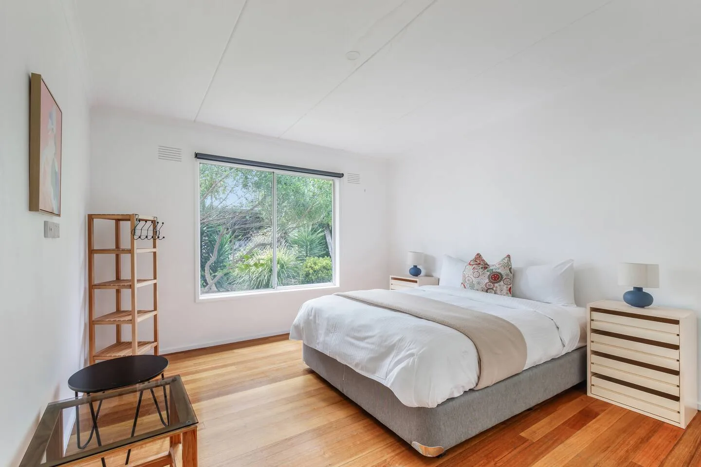 A bedroom with a bed beside a large window overlooking greenery.