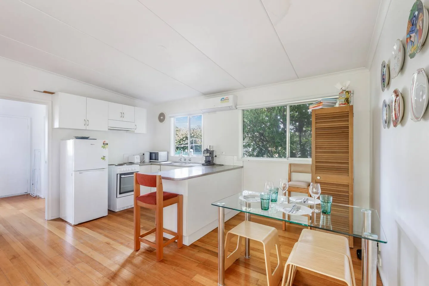 A bright kitchen and dining area with a glass table beside large windows.