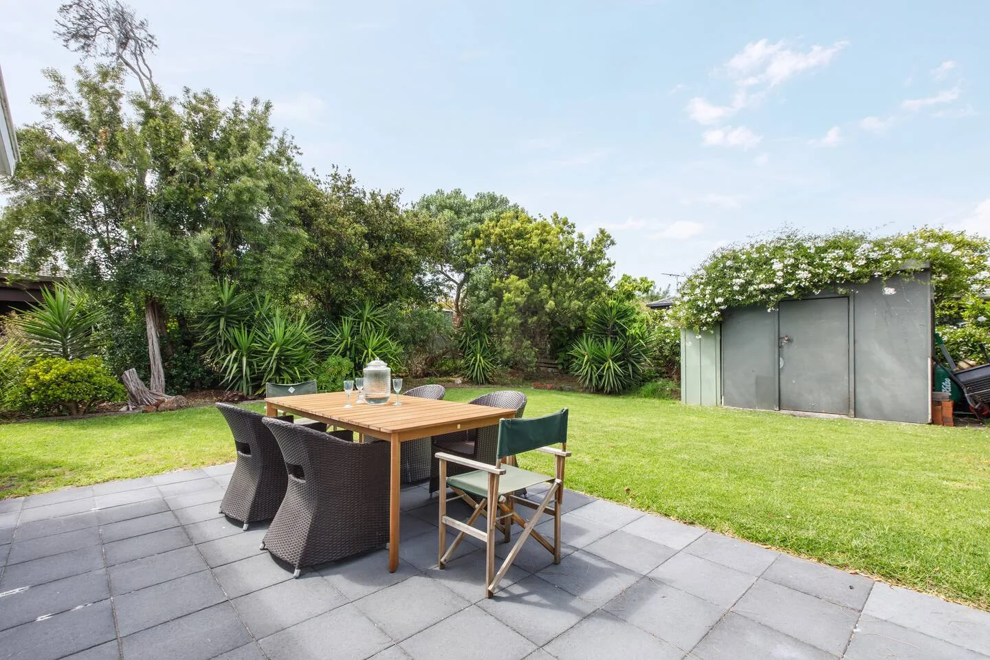 The paved patio offers an easygoing outdoor dining experience with comfortable seating set beside leafy surrounds.