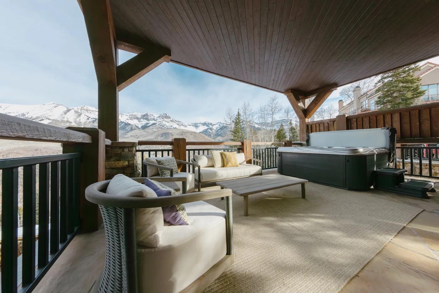 Una zona cubierta de estar al aire libre da a montañas nevadas, con una bañera de hidromasaje junto a la terraza.