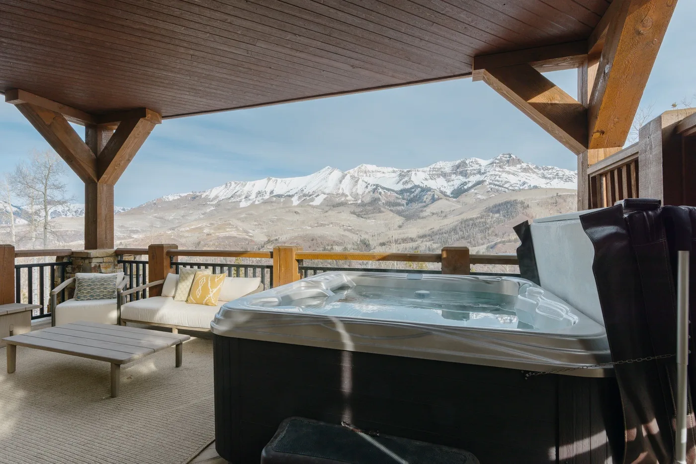 Una terraza exterior cubierta con jacuzzi y asientos ofrece vistas a montañas nevadas.