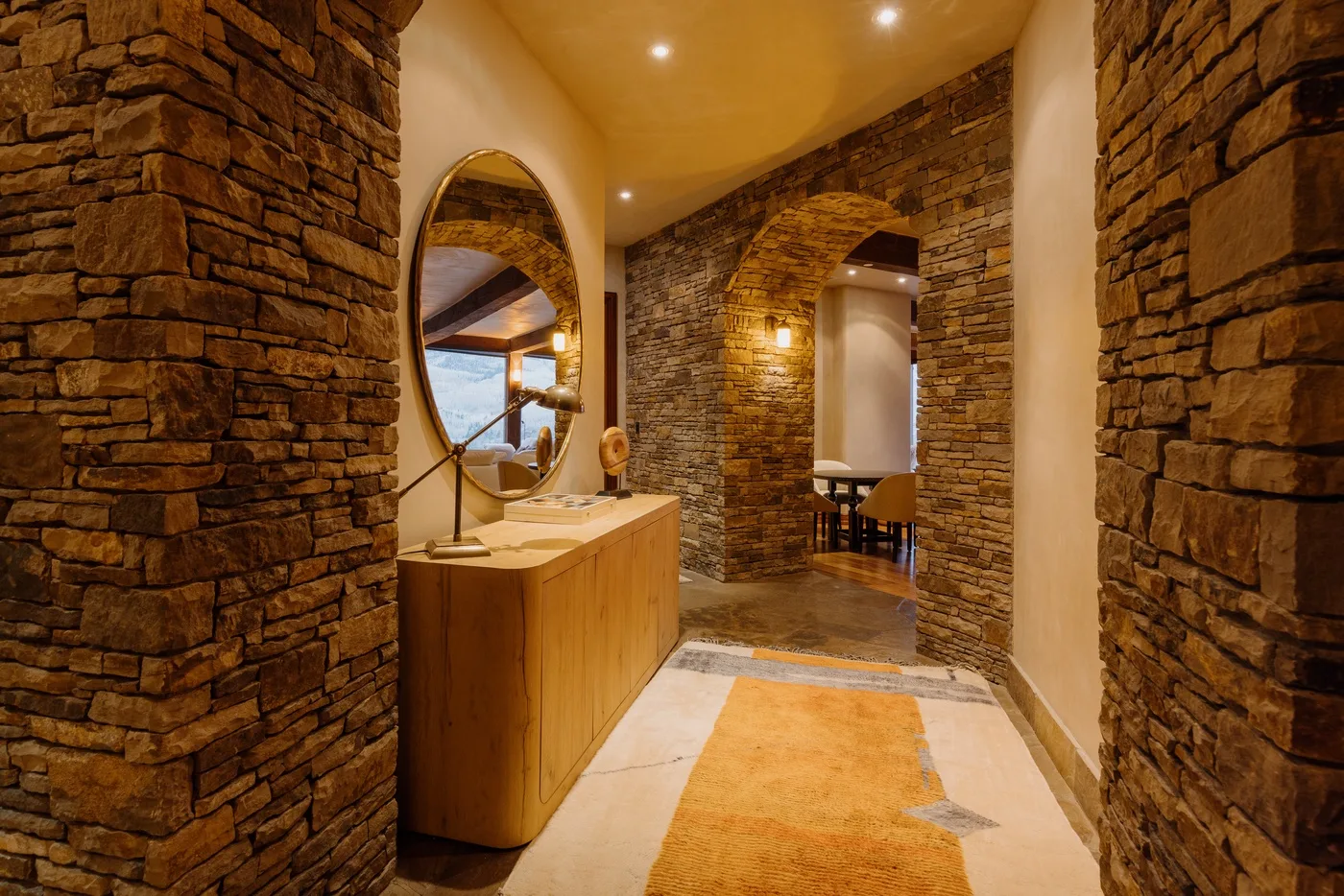 Pasillo de piedra con iluminación cálida, un mueble de madera y un arco.
