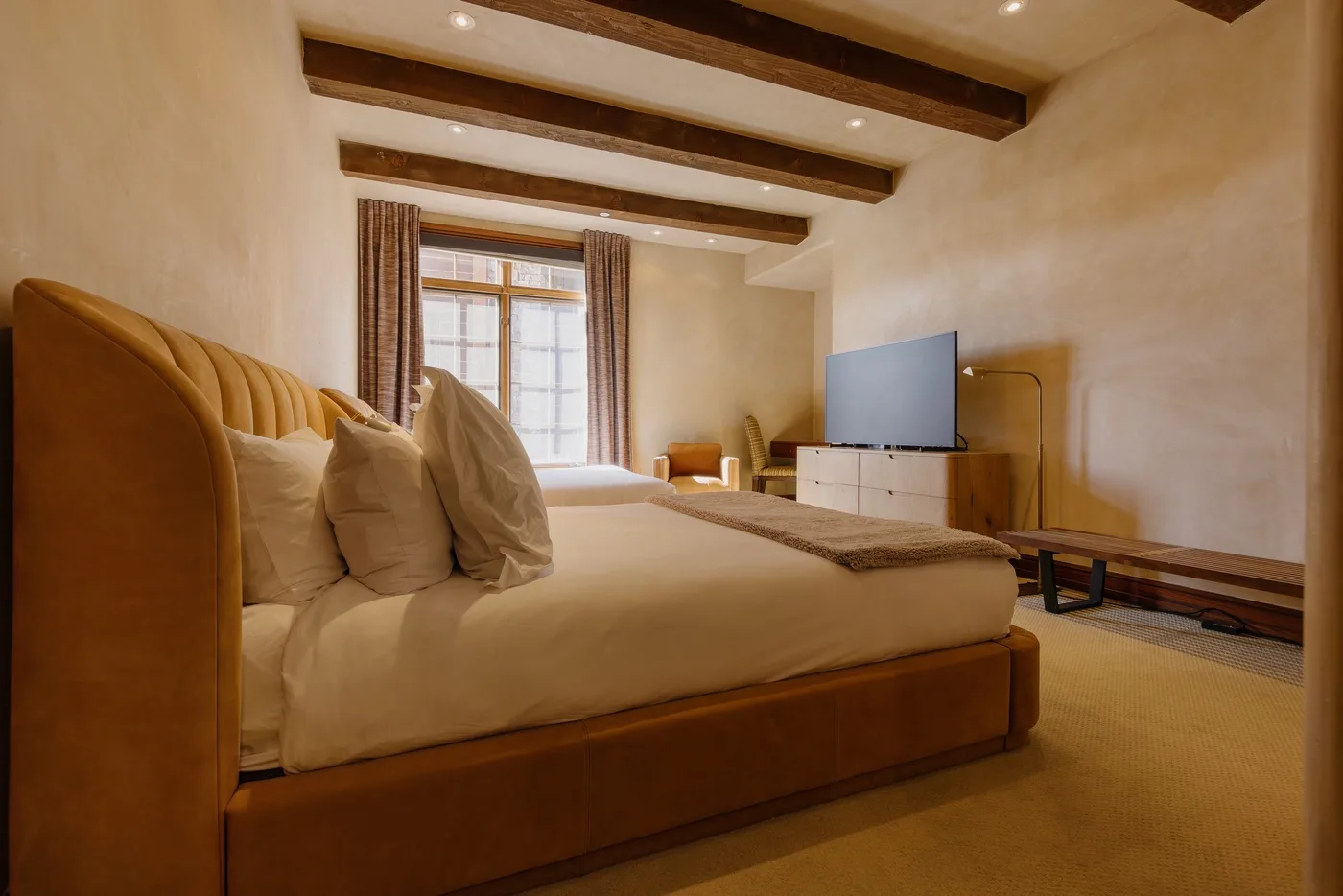 Un dormitorio con una cama, un televisor y vigas a la vista en el techo.