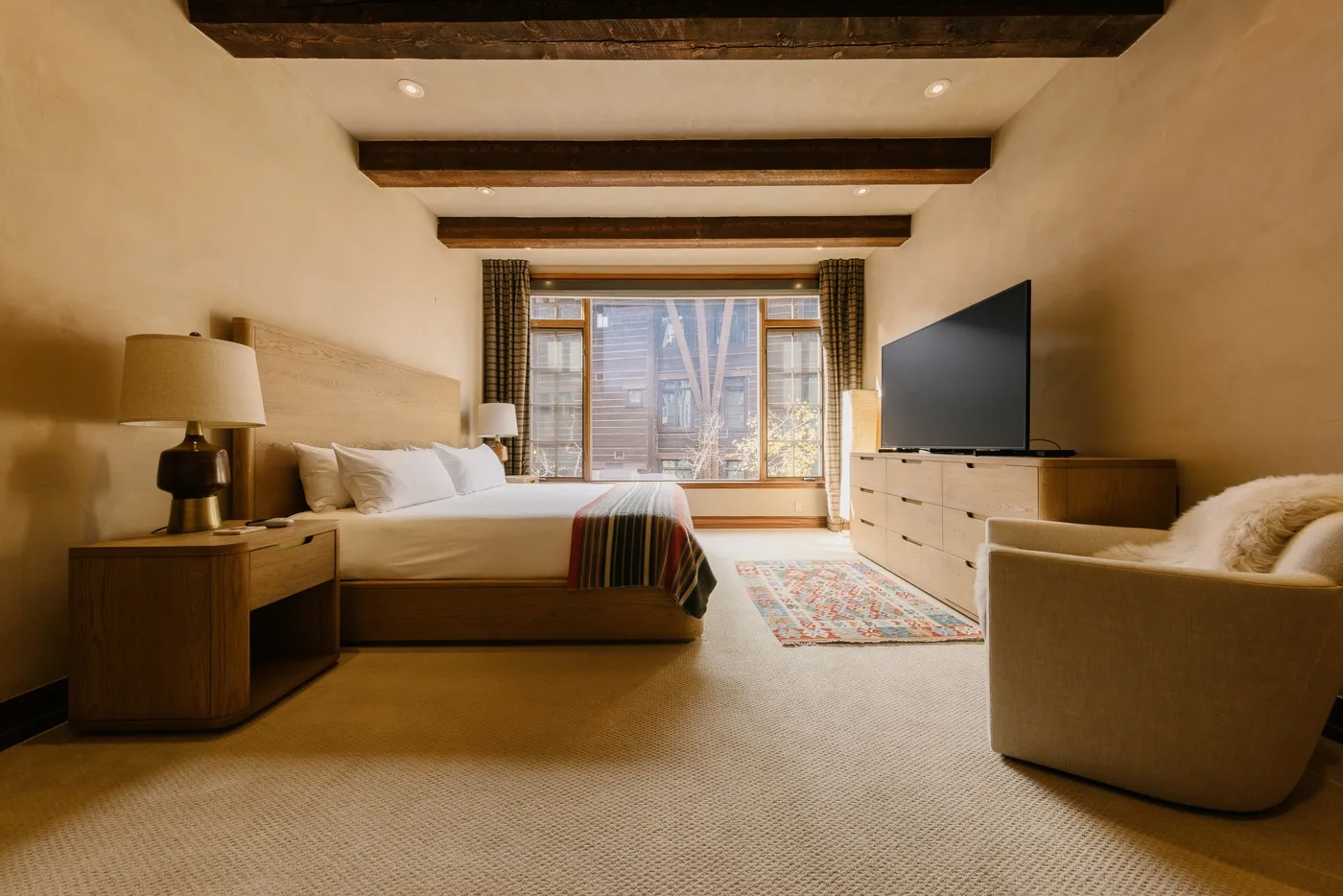 Un dormitorio con una cama, asientos y un televisor junto a una ventana amplia.