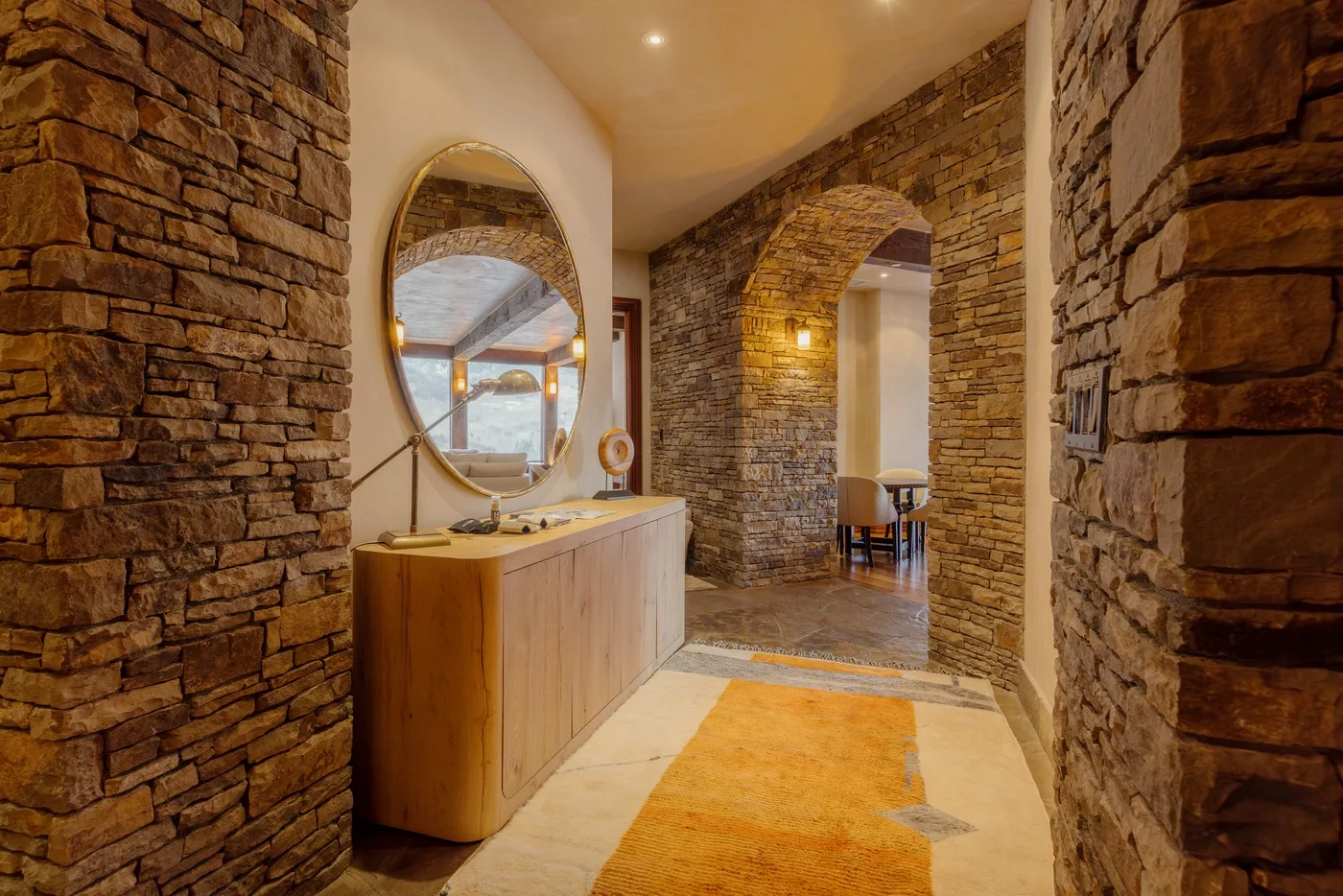 Un pasillo interior de paredes de piedra pasa junto a una consola de madera y un arco.