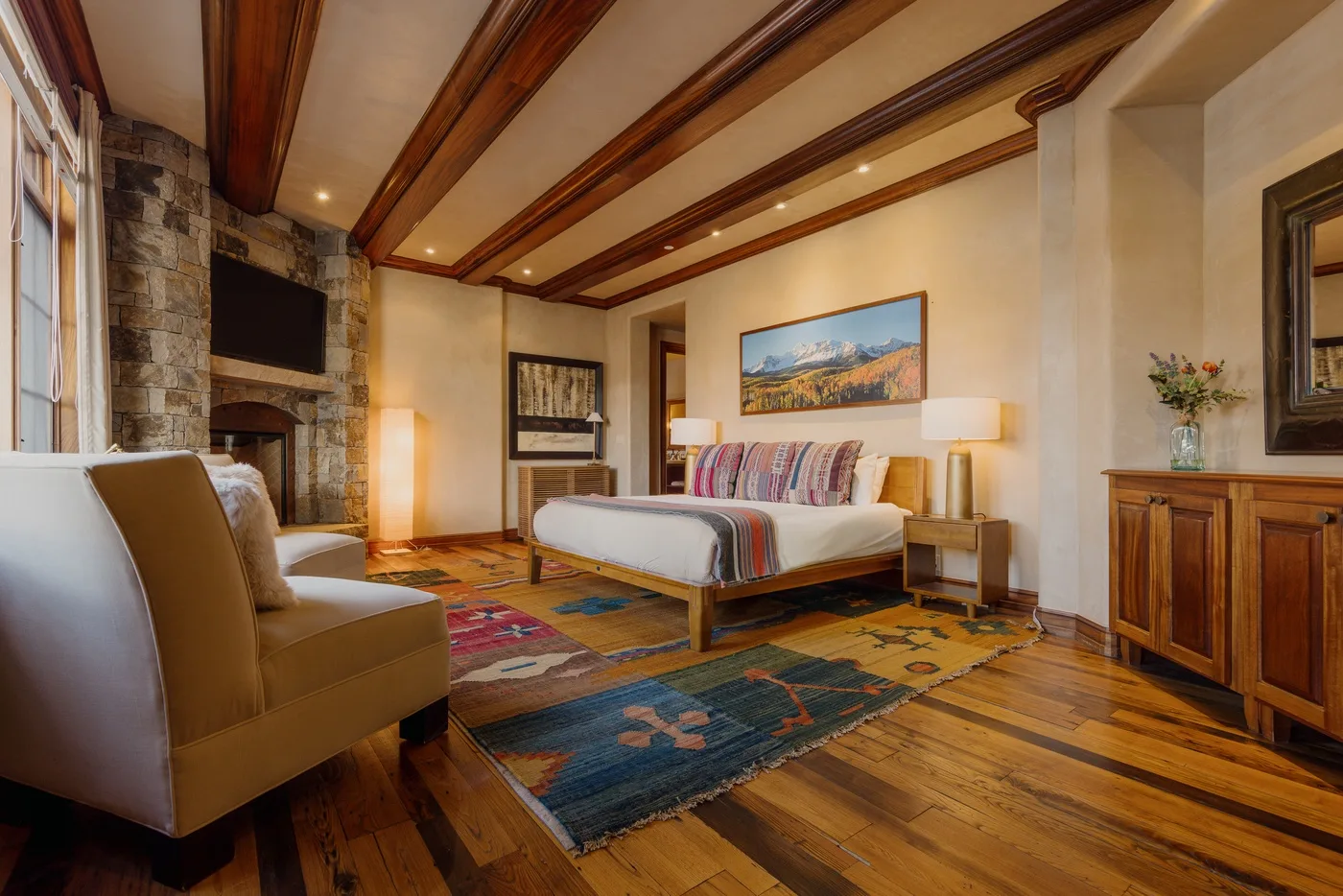 Un dormitorio con cama, asientos y una chimenea de piedra bajo vigas de madera expuestas.