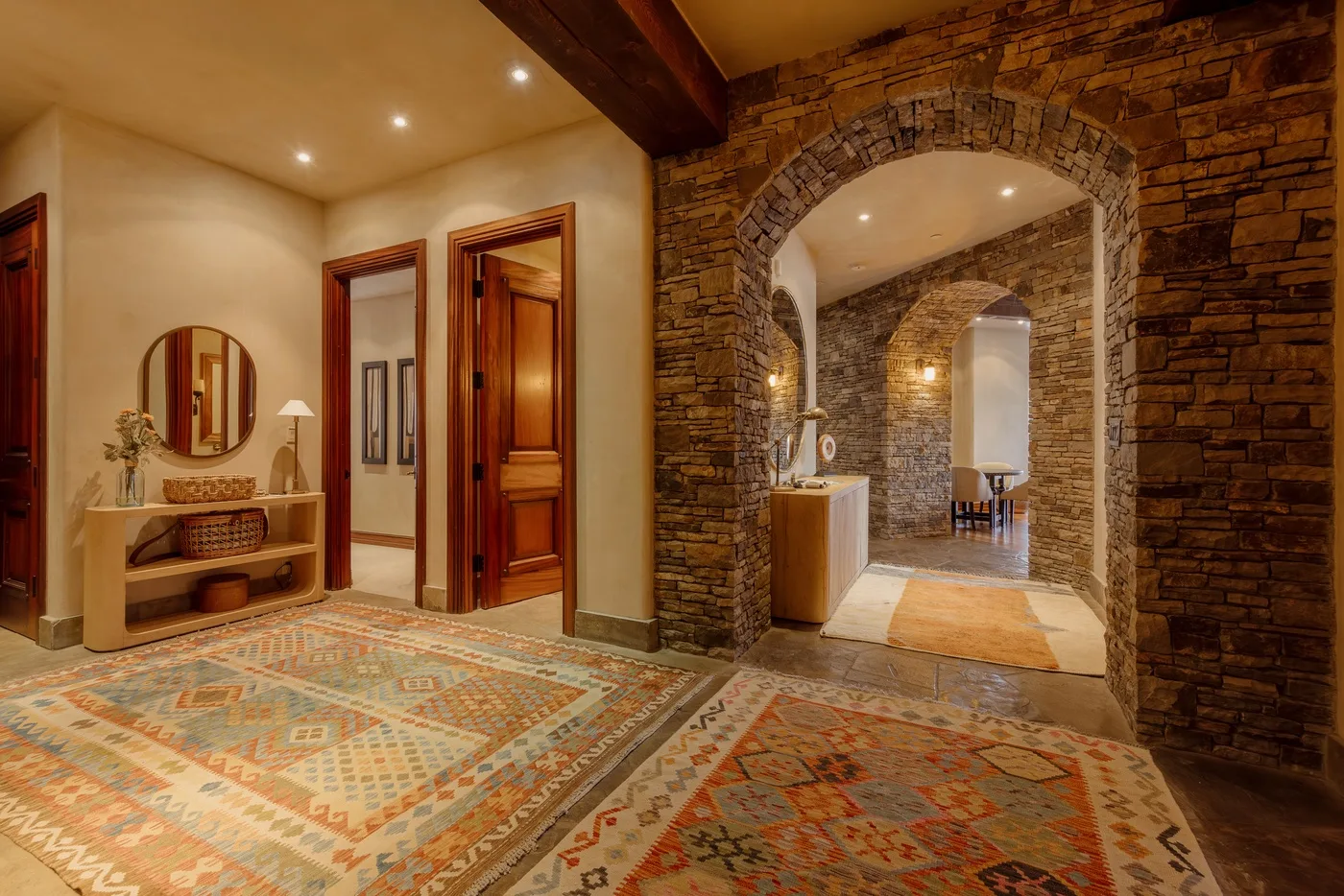 Un pasillo con arco de piedra da a una sala con alfombras estampadas y puertas de madera.