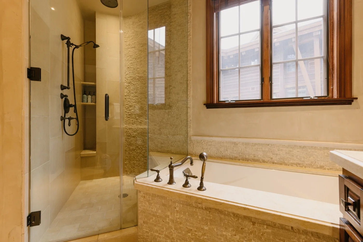 Un baño con una ducha de vidrio y una bañera bajo una ventana.