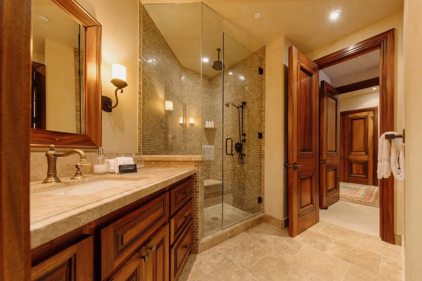 Un baño con un tocador largo y una ducha de vidrio junto a una puerta abierta.