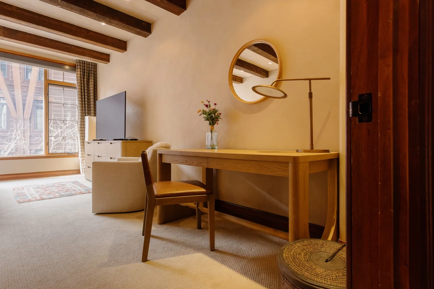 Un cálido espacio de trabajo en un dormitorio con escritorio de madera, silla y espejo redondo.