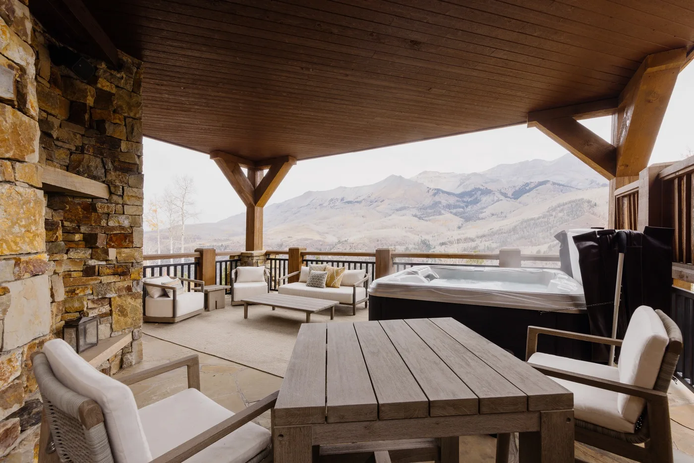 Un patio cubierto tiene asientos, una mesa y una bañera de hidromasaje con vista a las montañas.