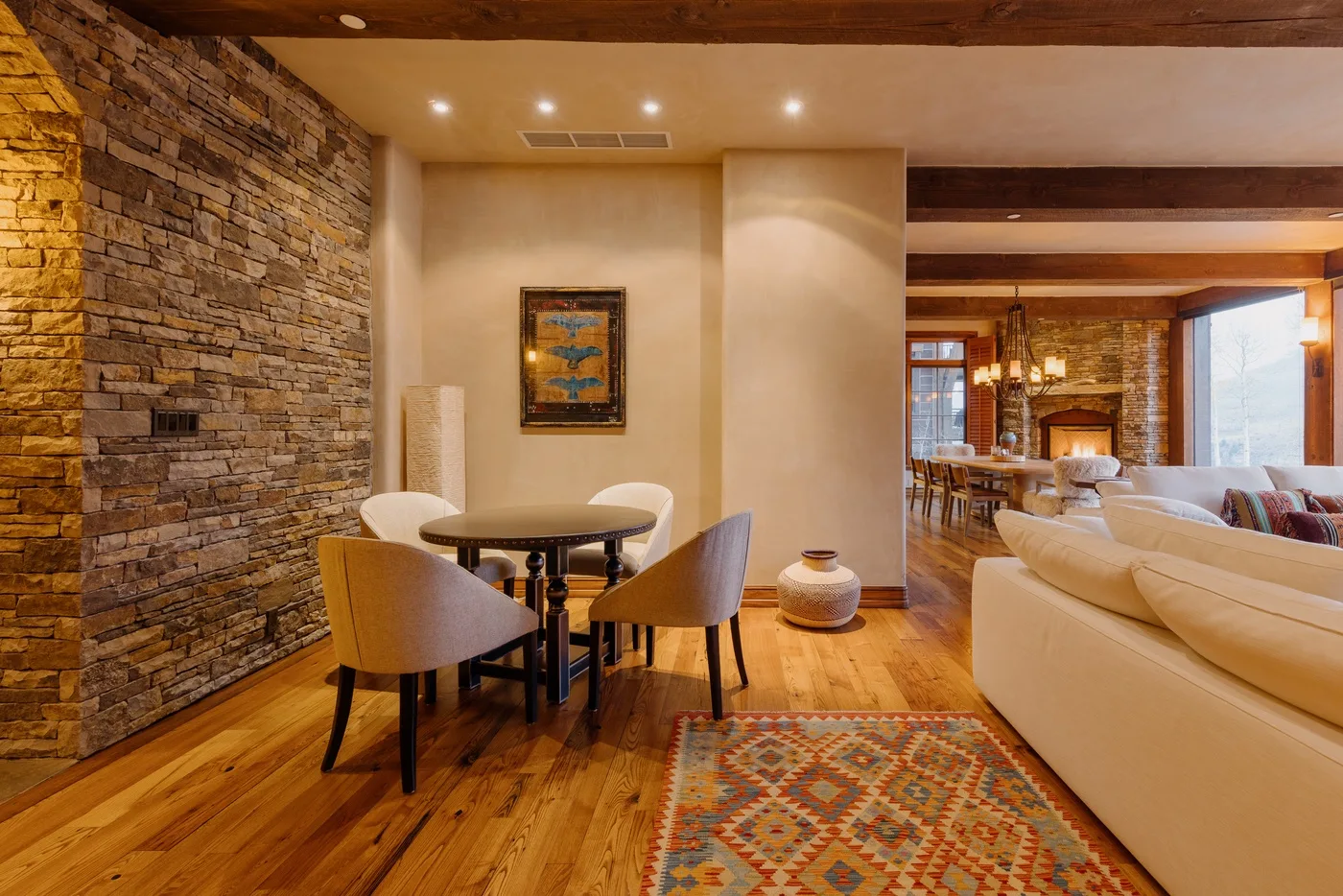 Una cálida sala de estar y comedor con una pared de piedra y una alfombra estampada.