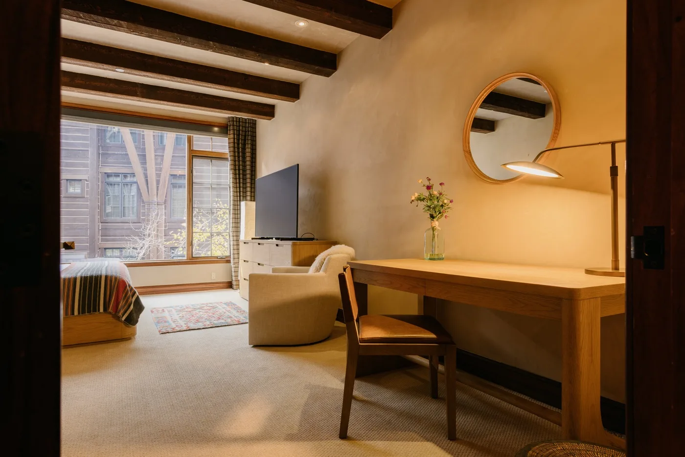 Dormitorio y zona de escritorio con una silla, televisor y ventana grande.