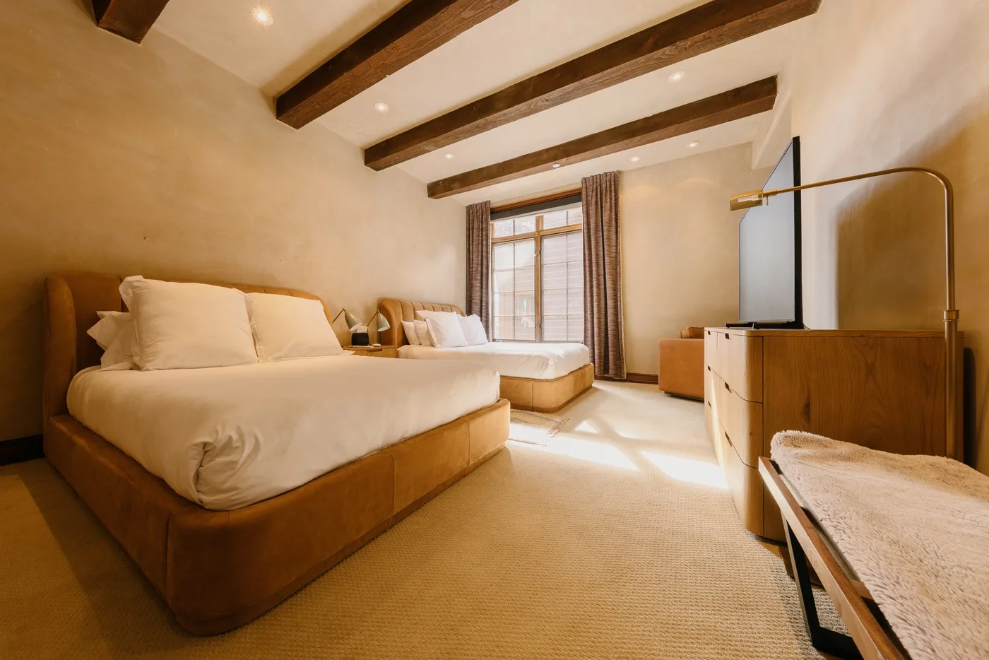 Un dormitorio con dos camas, una ventana con cortinas y vigas expuestas en el techo.