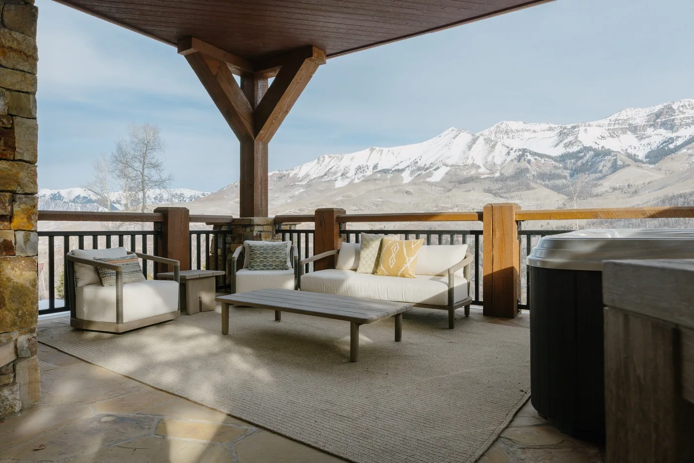 Un patio cubierto tiene asientos acolchados y vistas a montañas nevadas.