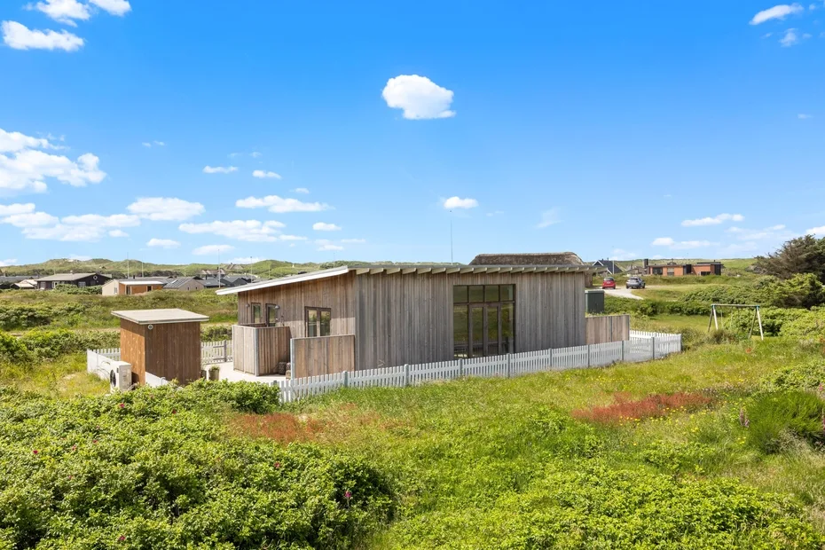 A low modern building sits among grassy fields beneath a bright blue sky.