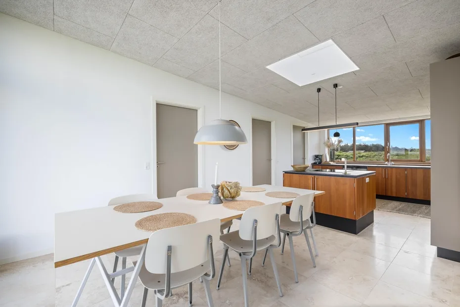 A bright dining area with a long table and an open kitchen beyond.