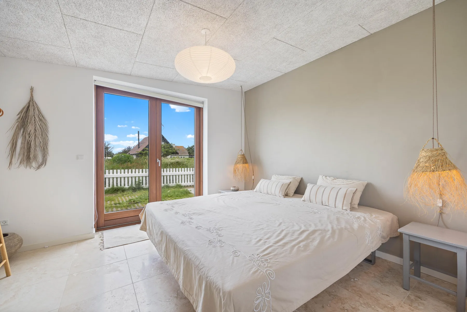 A bright bedroom with a large bed and glass doors opening to a garden.