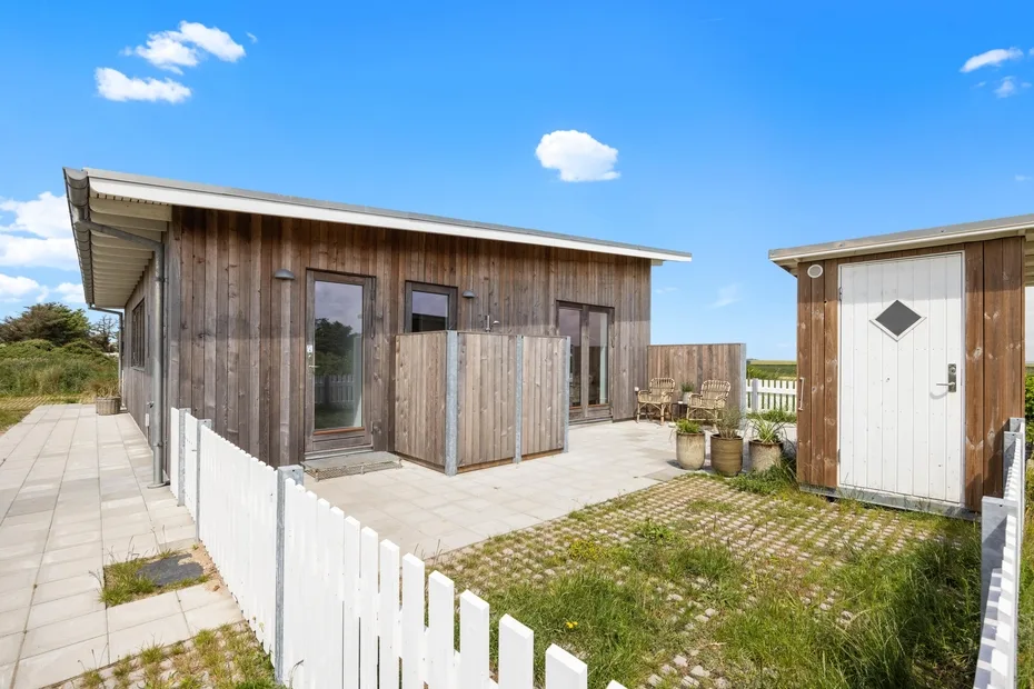 A wooden building opens onto a paved patio with a white fence.