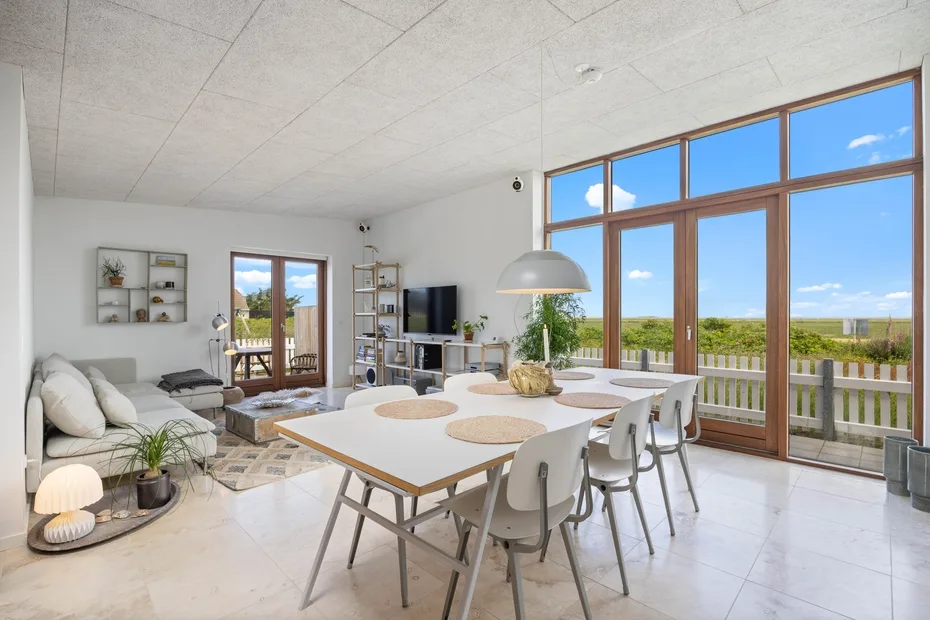 A bright open-plan living and dining area has large windows overlooking greenery.